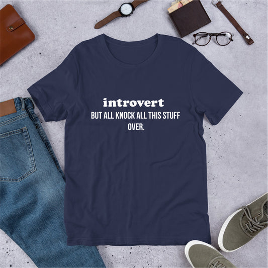 Navy blue t-shirt with 'introvert BUT ALL THIS STUFF OVER.' text on a gray surface with jeans, shoes, and accessories.