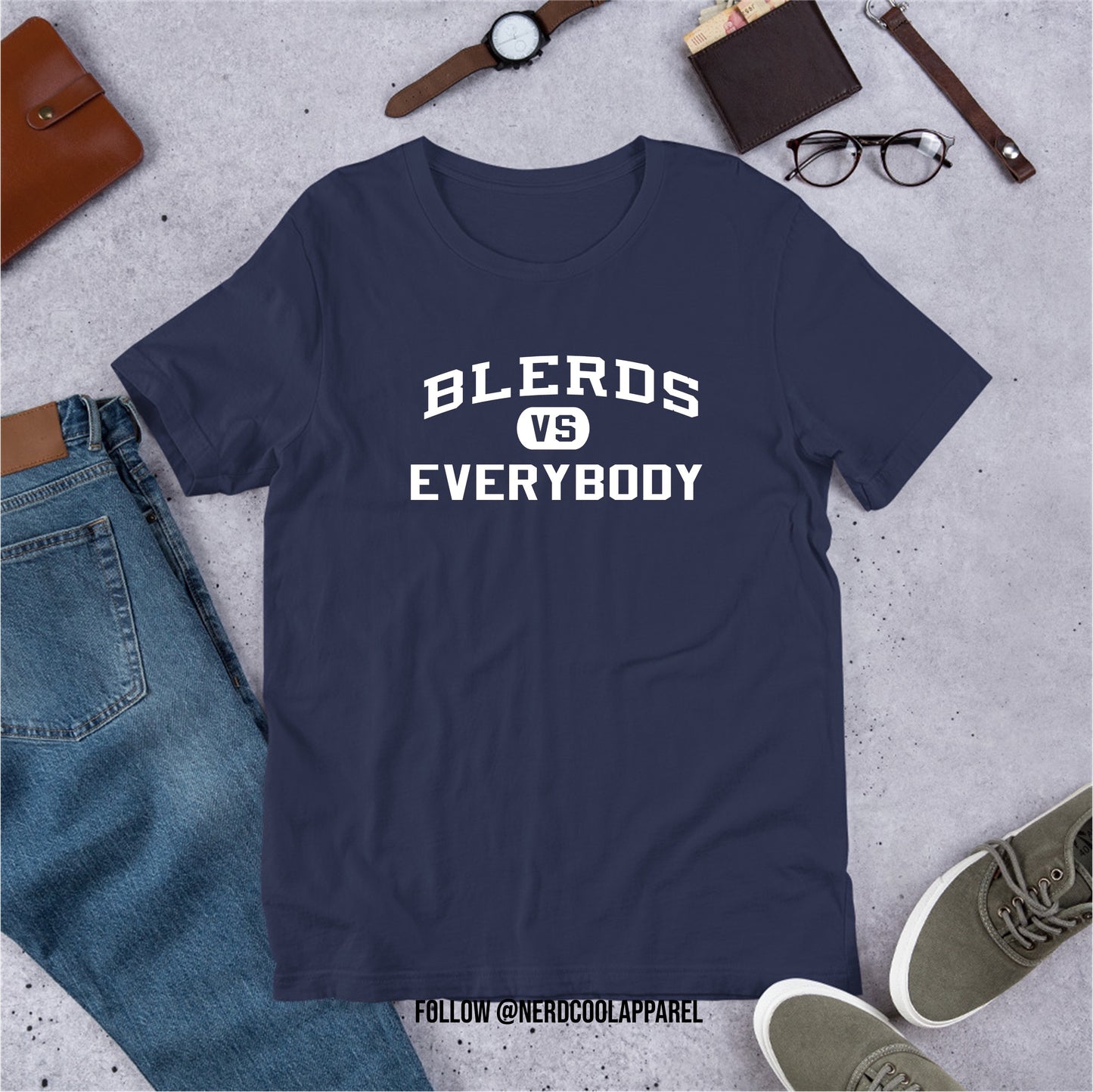 Navy blue t-shirt with 'BLERDS VS EVERYBODY' text on a gray surface with jeans, shoes, and accessories.