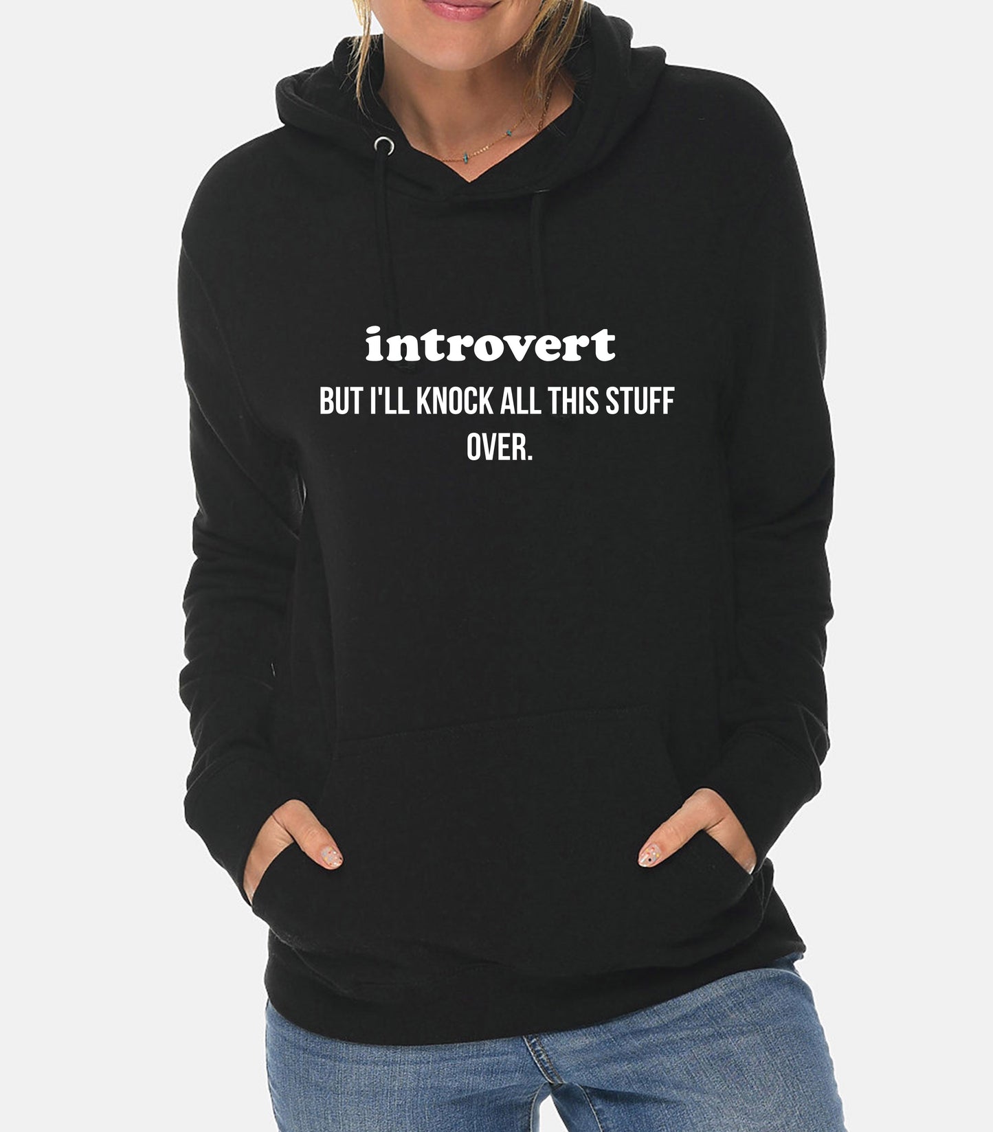 Person wearing a black hoodie with text 'introvert BUT I'LL KNOCK ALL THIS STUFF OVER.' on a plain background