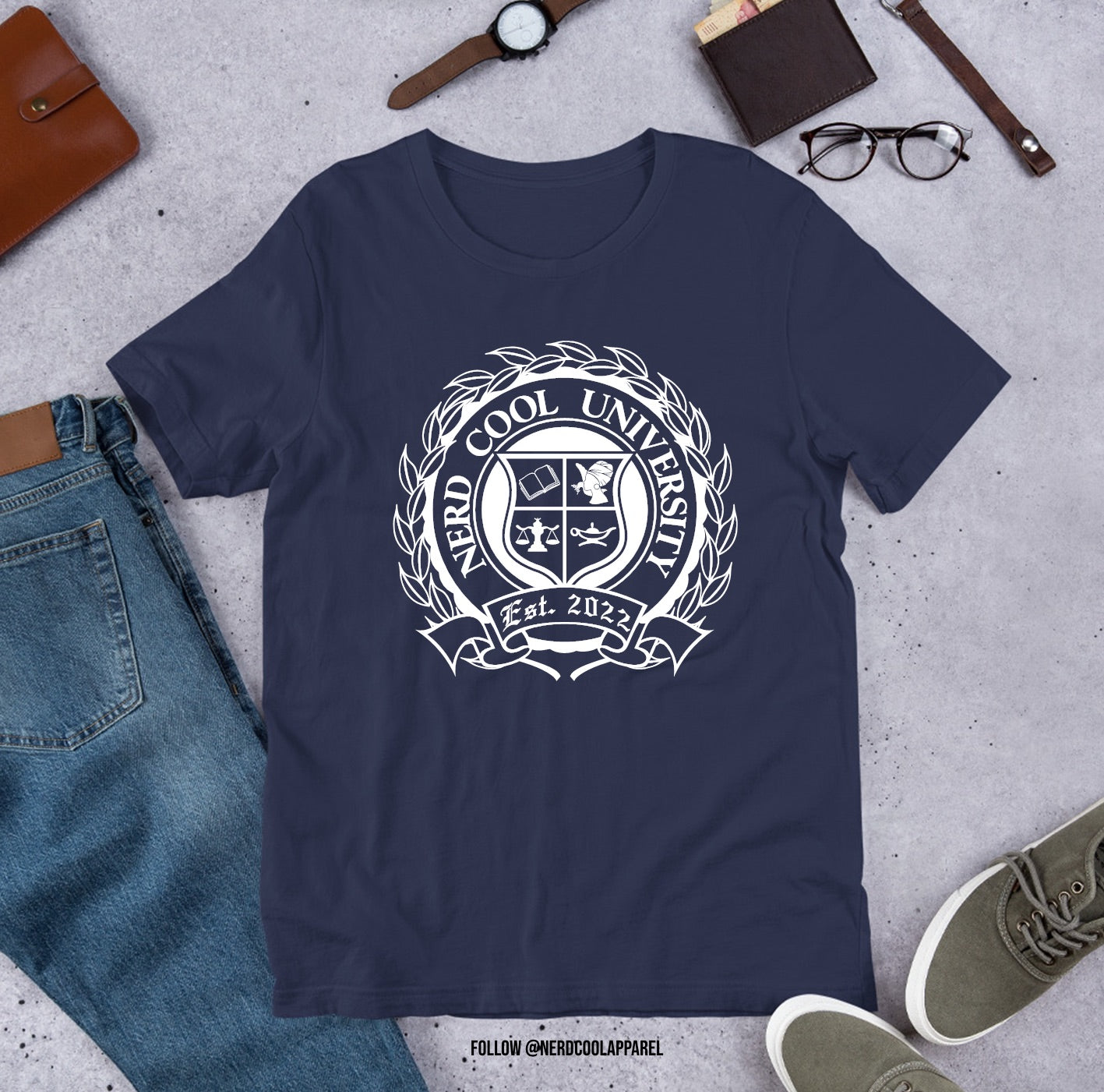 Navy blue t-shirt with 'New Cool University' logo on a gray surface with jeans, shoes, and accessories.