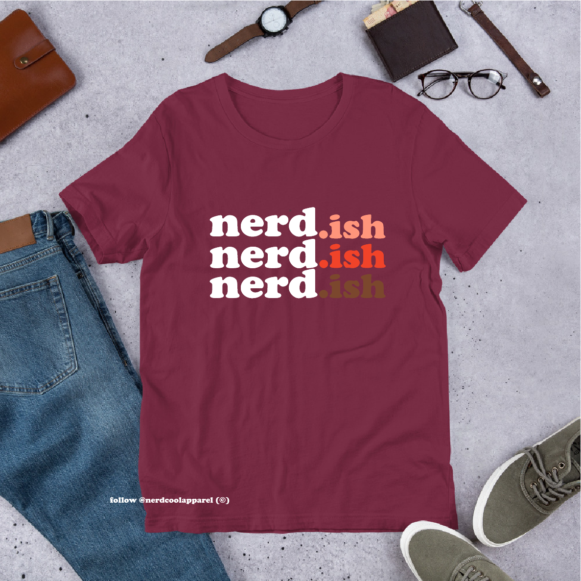 Maroon t-shirt with 'nerd.ish' text on a gray surface with casual items around