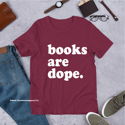 Maroon t-shirt with 'books are dope.' text on a gray surface with casual items.