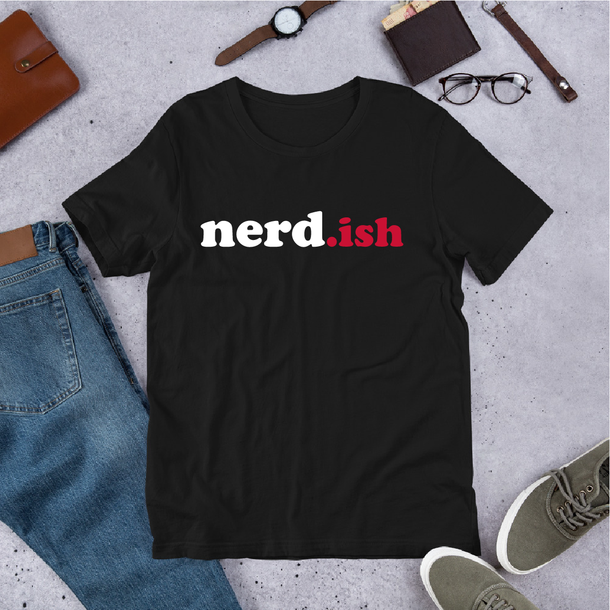 Black t-shirt with 'nerd.ish' text on a concrete surface with jeans, shoes, and accessories.