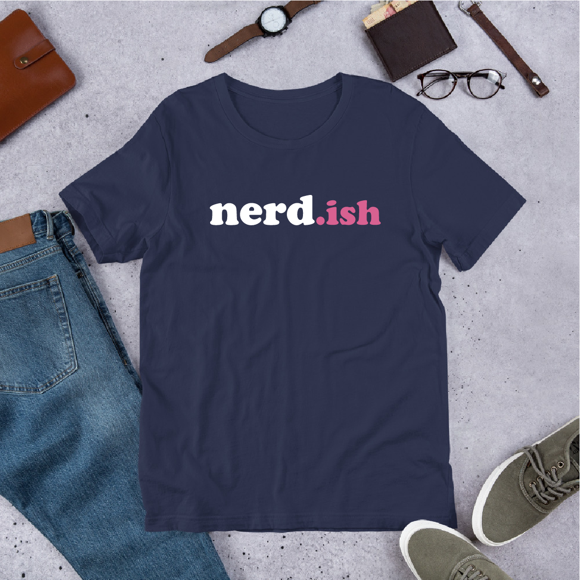 Navy blue t-shirt with 'nerd.ish' text on a concrete surface with jeans, shoes, and accessories.