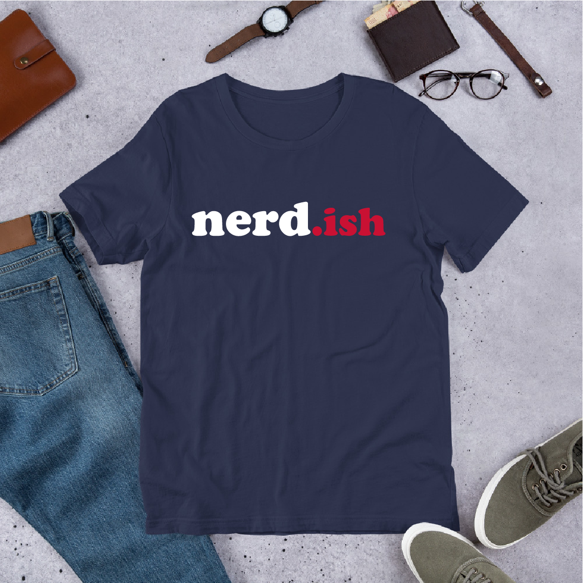 Navy blue t-shirt with 'nerd.ish' text on a gray surface with jeans, shoes, and accessories.