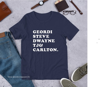 Navy blue t-shirt with white text on a gray surface with casual items around