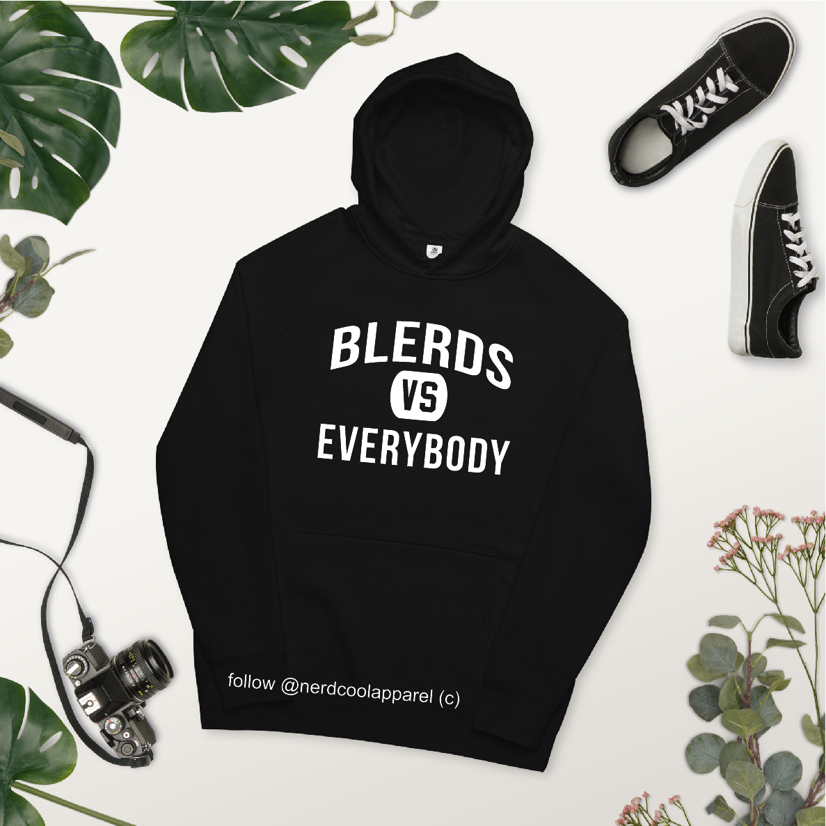 Black hoodie with 'BLERDS VS EVERYBODY' text, surrounded by plants and sneakers on a white background