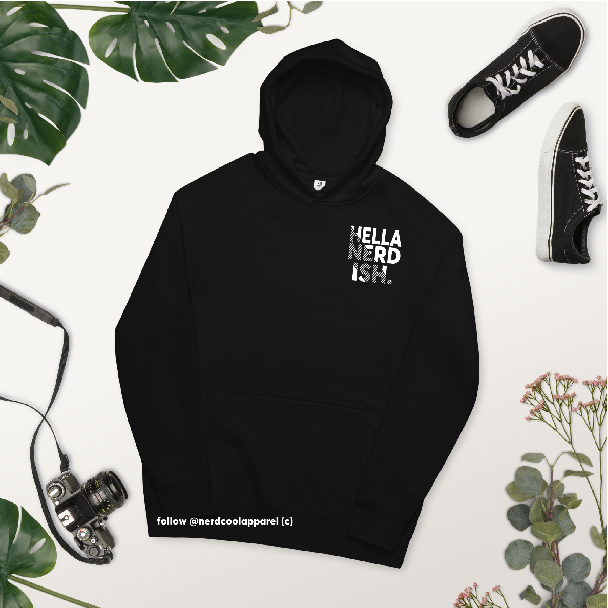 Black hoodie with 'Hella Nerd Ish' text, surrounded by plants and shoes on a white background