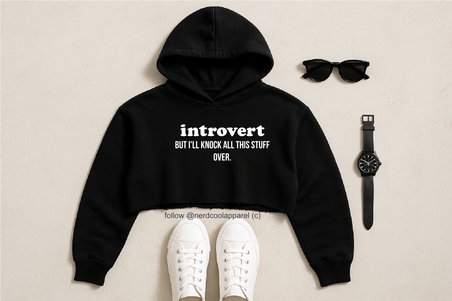 Black hoodie with 'introvert' text, white sneakers, sunglasses, and watch on a beige background