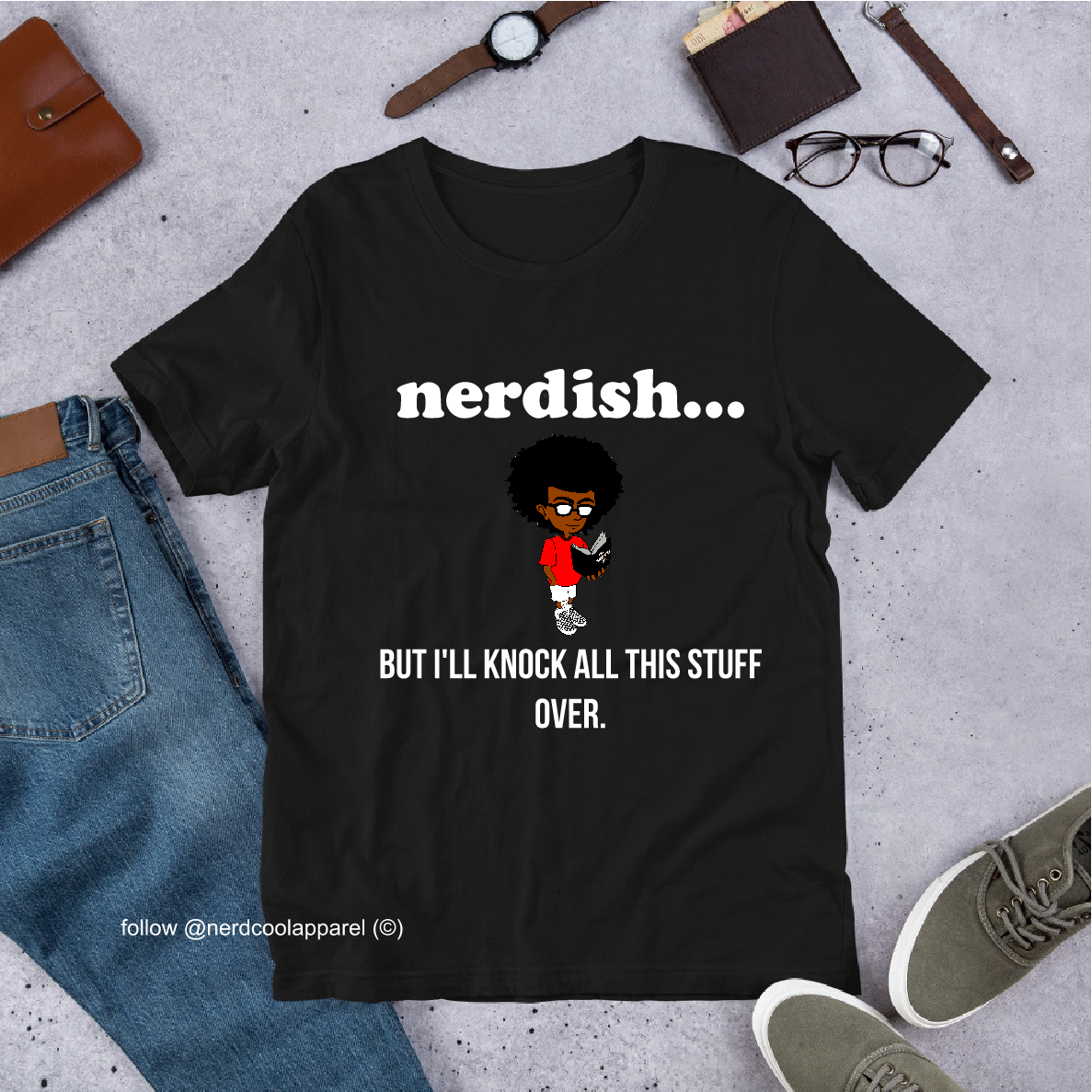 Black t-shirt with 'nerdish...' text and cartoon character, surrounded by jeans, shoes, and accessories on a gray surface.