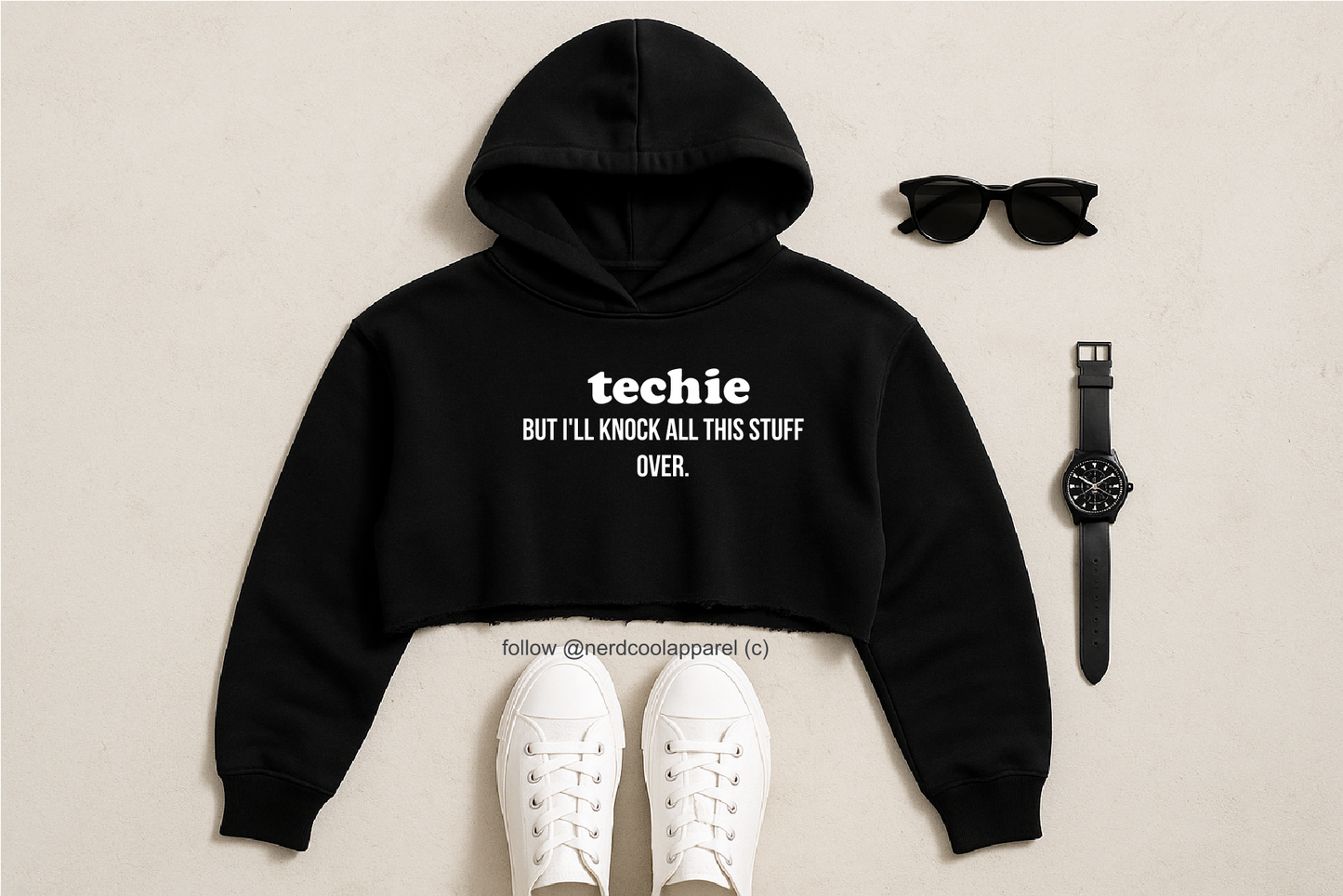 Black hoodie with text, white sneakers, sunglasses, and watch on a beige background