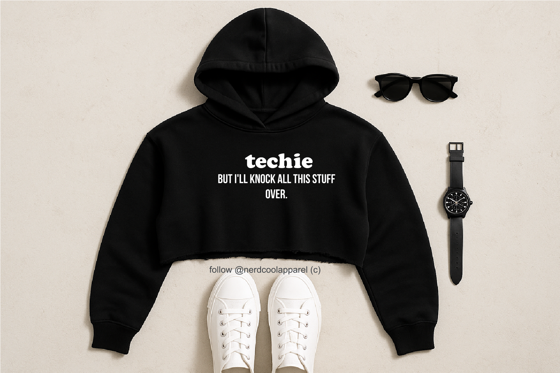 Black hoodie with text, white sneakers, sunglasses, and watch on a beige background