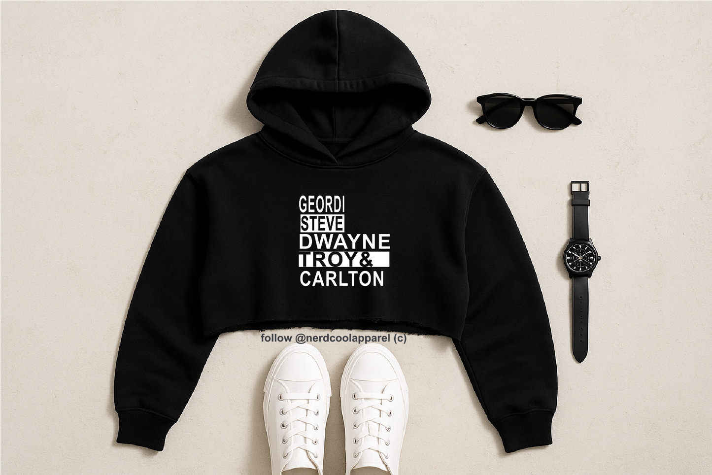 Black hoodie with text, white sneakers, sunglasses, and watch on a beige background